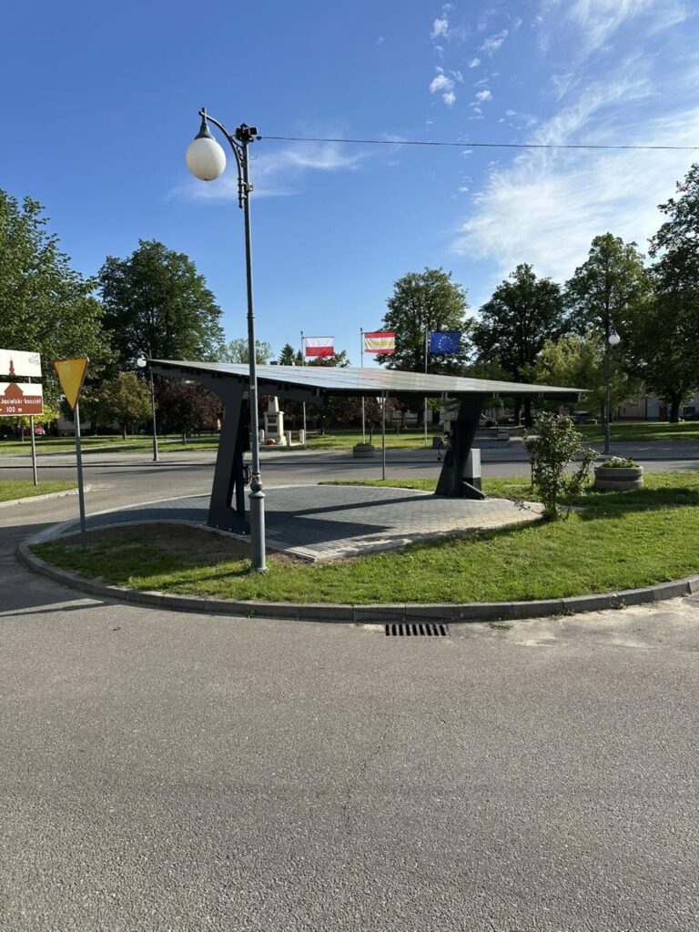 Carport elektryczny z ładowarką, w tle flaga Polski i Unii Europejskiej