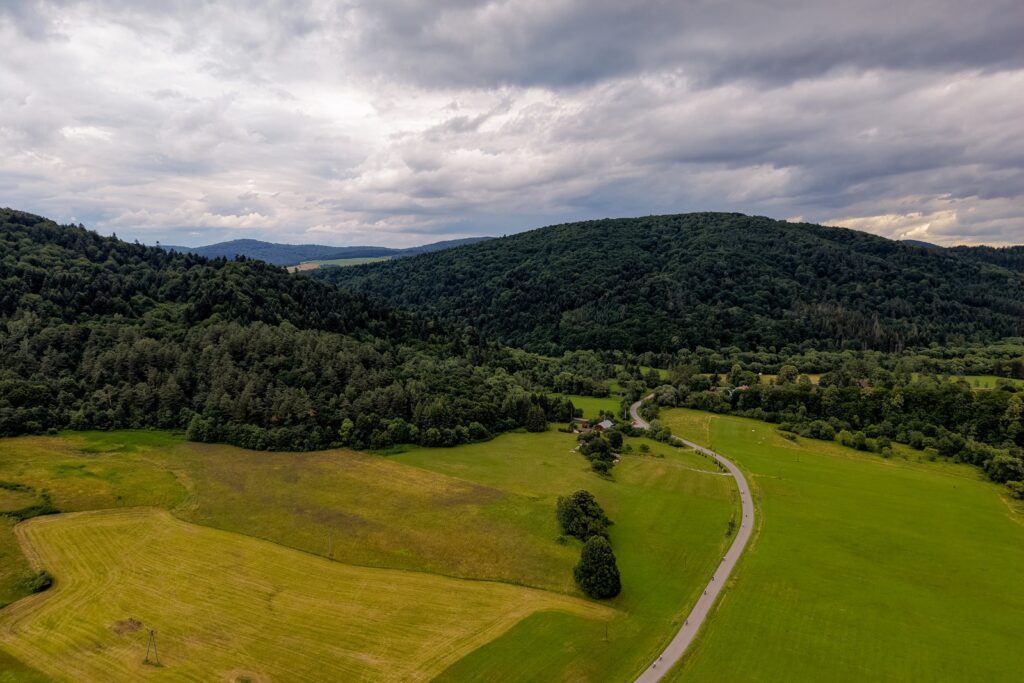 Widok z drona na rowerzystów jadących przez zieloną dolinę otoczoną lasami i wzgórzami