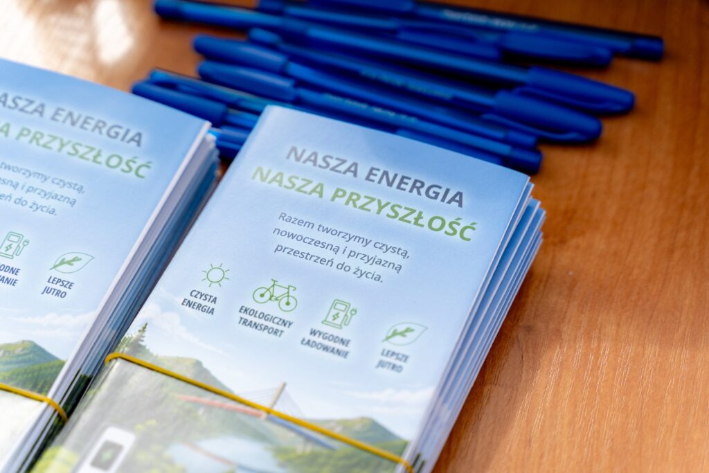 Ulotki z napisem „Nasza energia, nasza przyszłość” oraz stos niebieskich długopisów leżące na drewnianym stole.