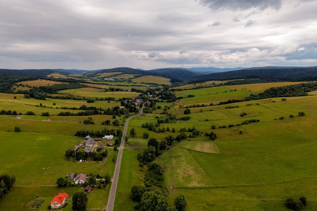 Widok z drona na wieś pośród zielonych pól i wzgórz