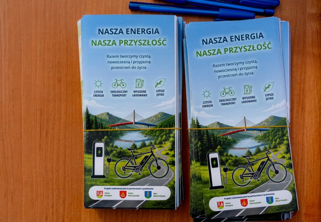 Dwa stosy ulotek „Nasza energia, nasza przyszłość” leżące obok siebie na drewnianym stole, w tle niebieskie długopisy.