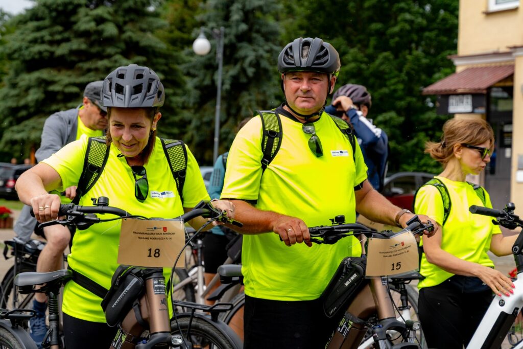 Dwoje rowerzystów w żółtych koszulkach odblaskowych z tabliczkami startowymi, trzymających kierownice rowerów.
