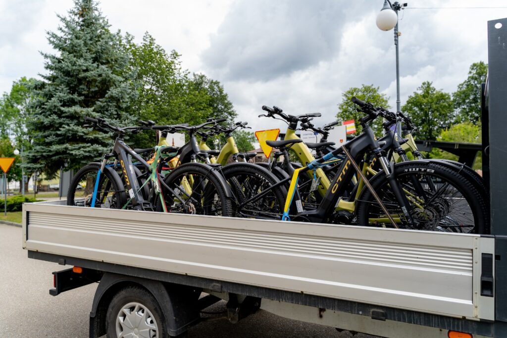 Rowery elektryczne przewożone na przyczepie samochodu, przypięte pasami transportowymi.