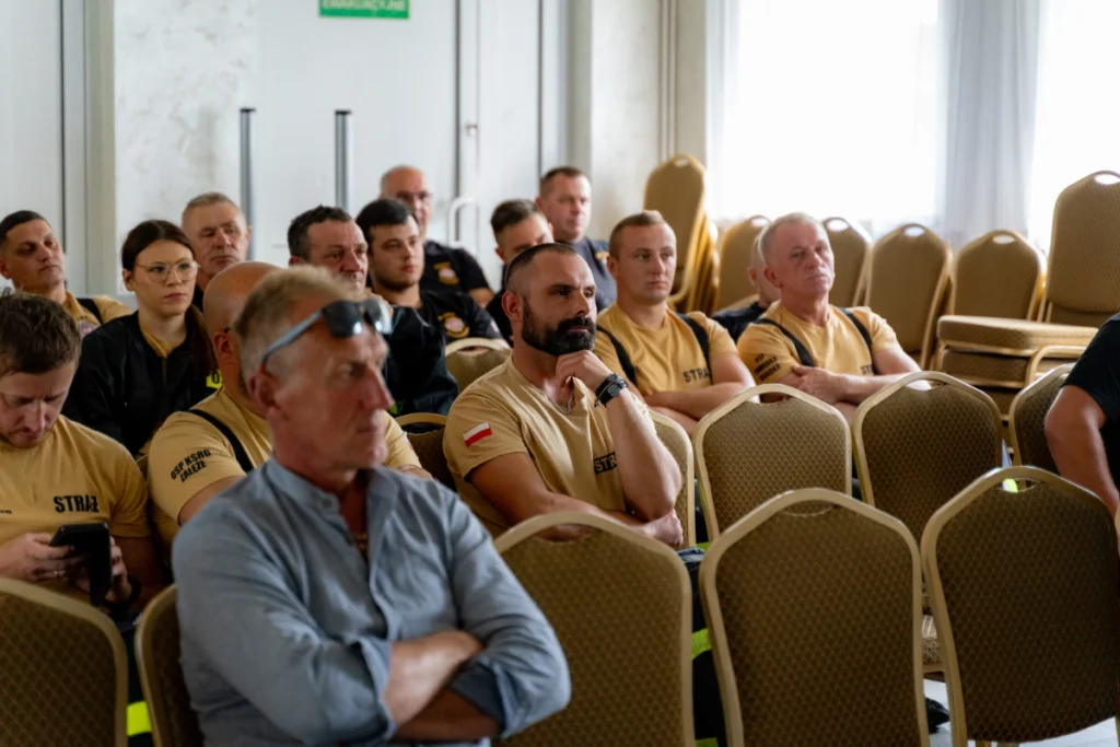Volunteer firefighters in sand-coloured shirts and other participants listen to the training, empty chairs in front of them