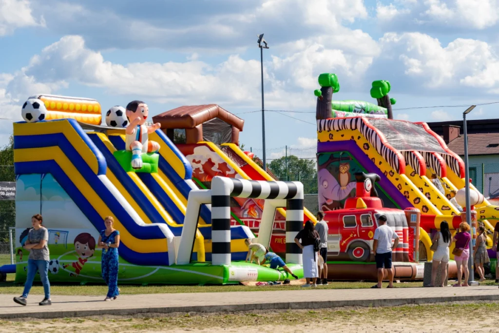 A row of bouncy castles, including a footballer-figure slide and an inflatable fire engine, parents with children nearby