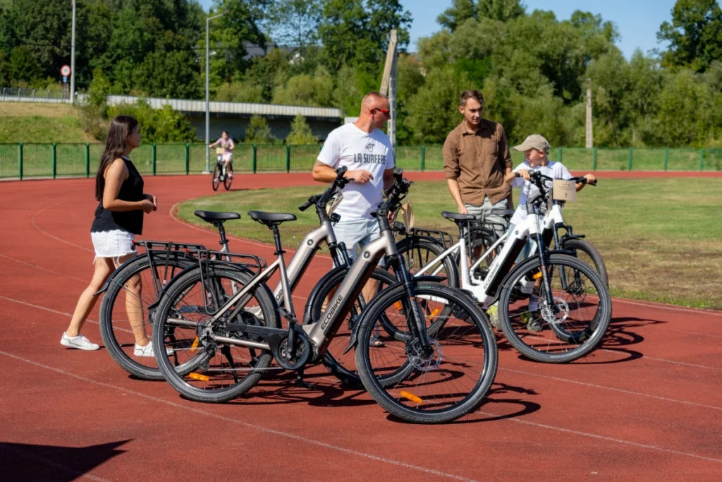 Participants stand by electric bikes on the red stadium running track, a boy with number 7 astride one