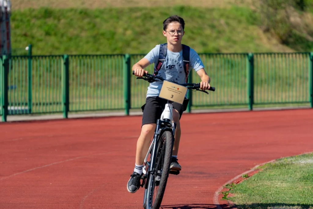 A teenager with a backpack rides an electric bike bearing number 3 along the red stadium running track