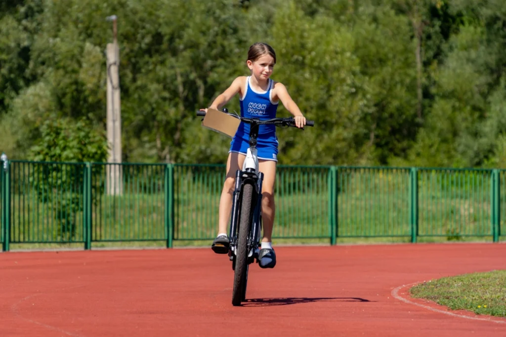 A girl in blue sportswear rides an electric bike straight ahead on the red stadium running track