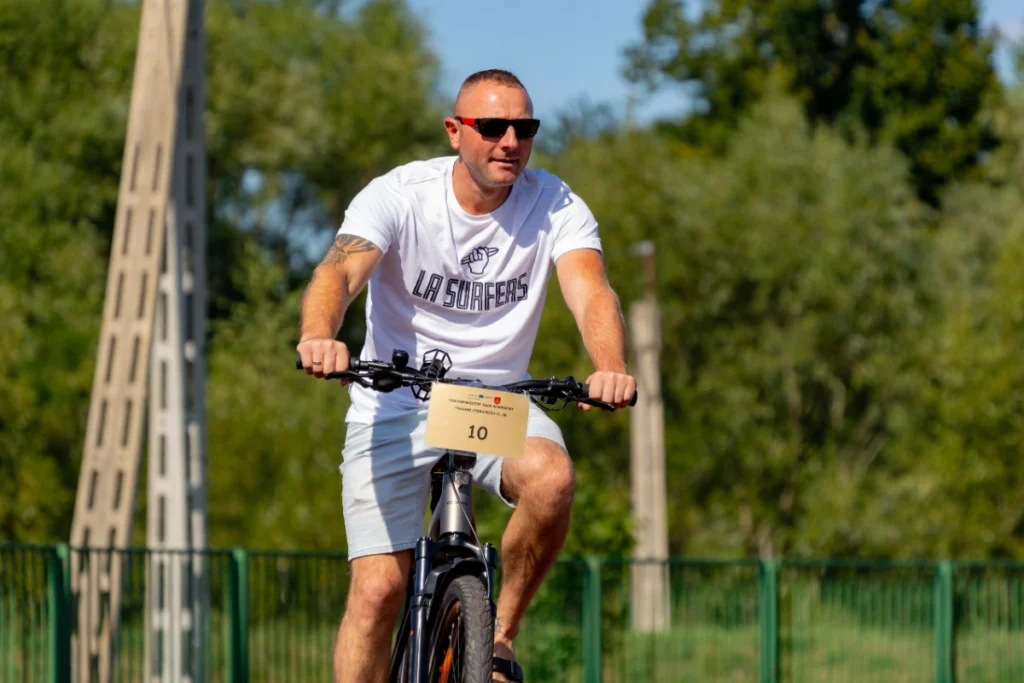A man in a white T-shirt rides an electric bike with race number 10 along the stadium fence