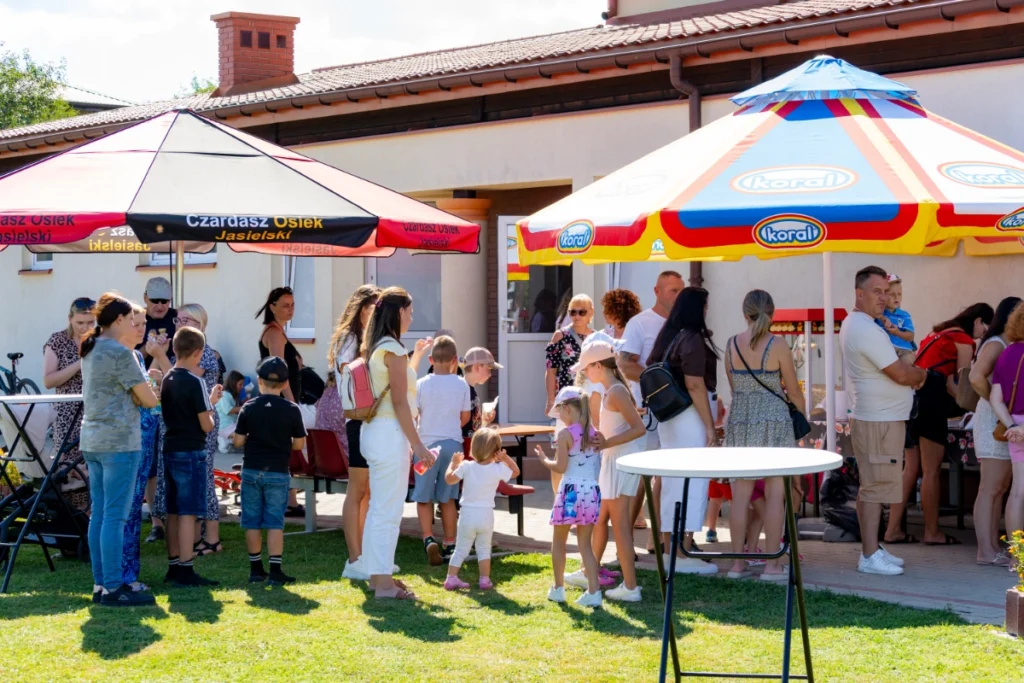 A queue of families with children at stalls under parasols marked Czardasz Osiek Jasielski and Koral
