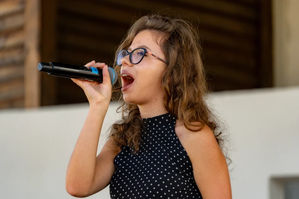 The youth band's vocalist sings with her mouth wide open, holding the microphone in one hand