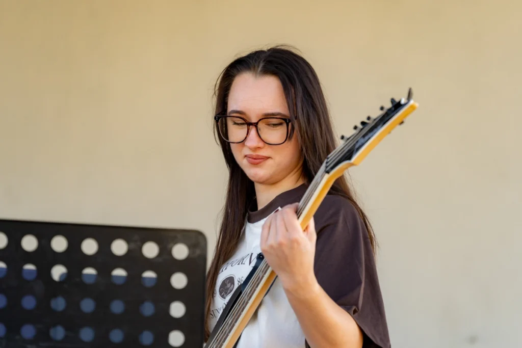 The band's bassist plays bass guitar, looking at the fretboard, with a black music stand beside her