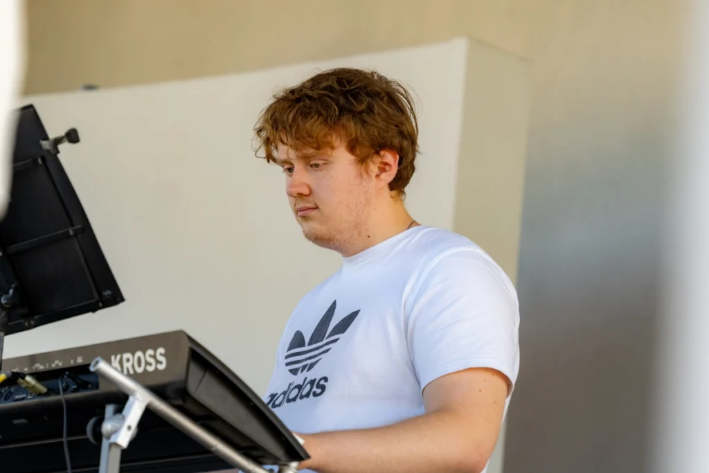The band's keyboardist plays a keyboard marked KROSS, with a music stand beside it