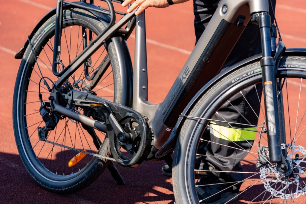 Close-up of a graphite ECOBIKE electric bike with an in-frame battery, held by hand on the red track