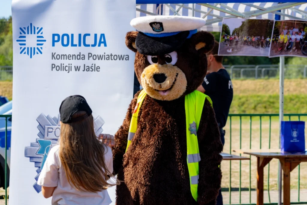 A girl greets the police bear mascot beside the Jasło County Police banner