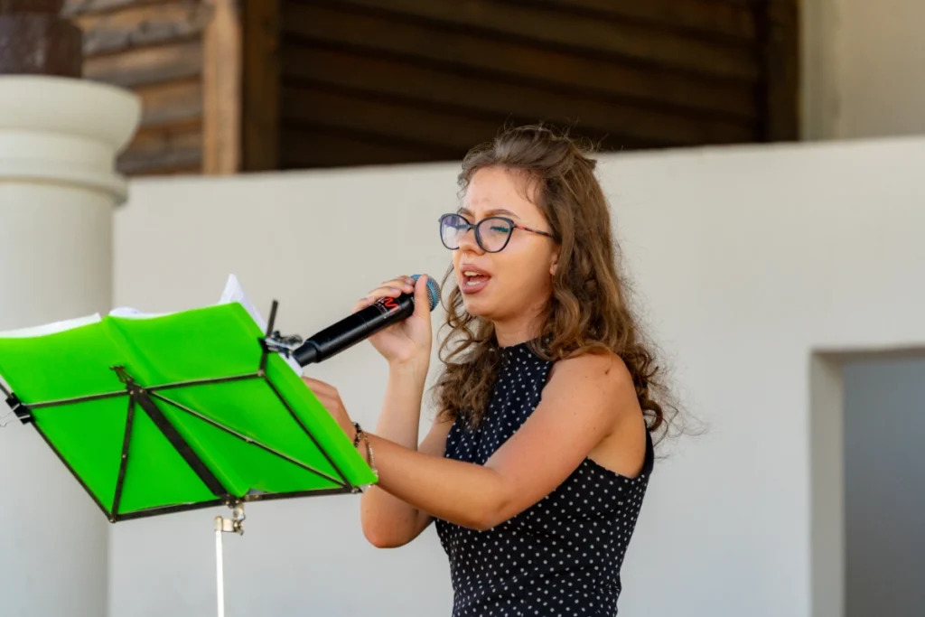 The band's vocalist sings into the microphone, holding her pages in place on a green music stand