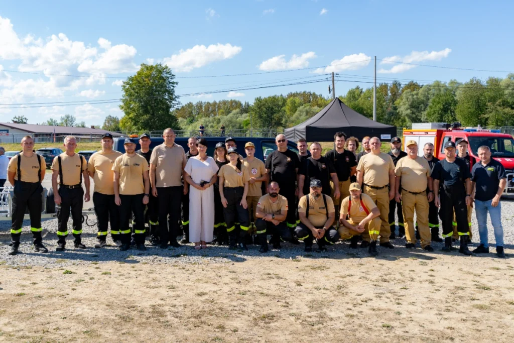 Volunteer firefighters in sand-coloured and black uniforms pose for a group photo in front of a black tent