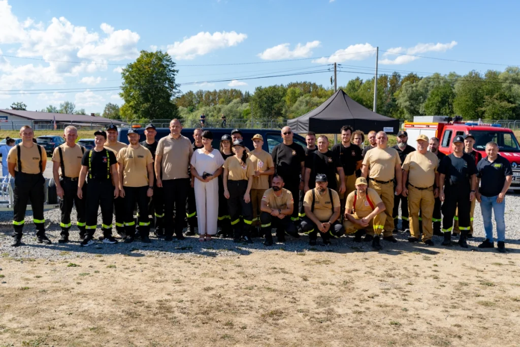 Volunteer firefighters in two rows pose for a group photo, with a red fire engine on the right