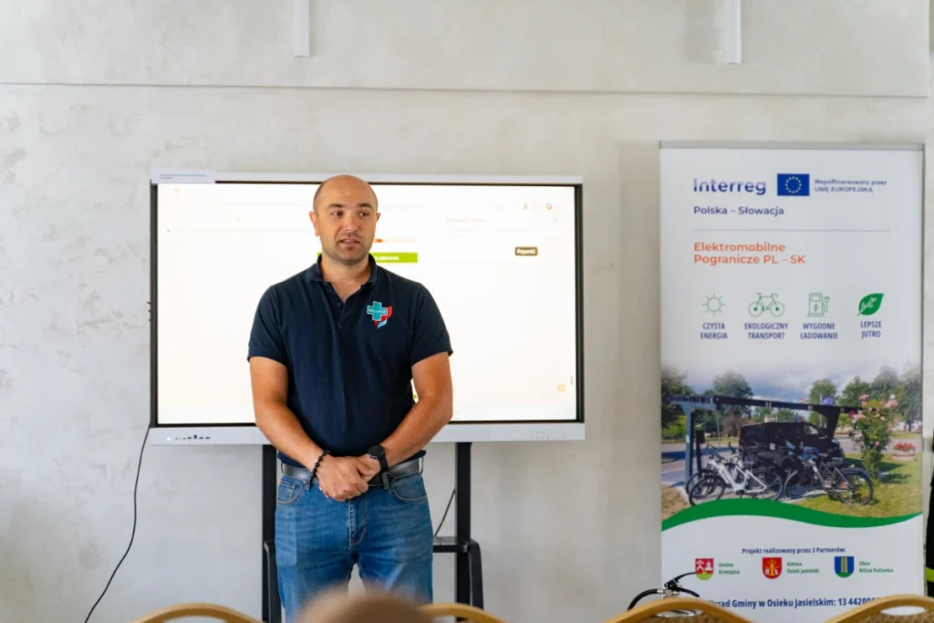 Training instructor in a navy polo shirt speaks by a large screen beside an Interreg project roll-up banner