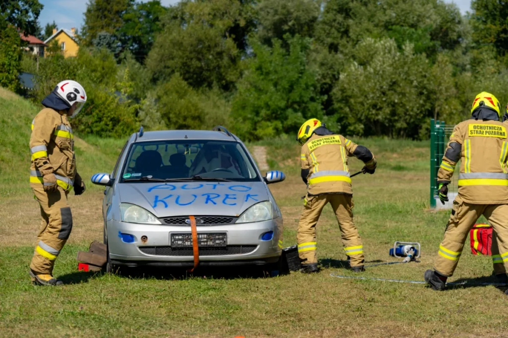 Volunteer firefighters prepare a silver car marked AUTO KUREK for the demonstration, a hydraulic rescue tool lying nearby