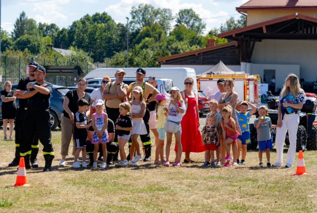 Children with parents and black-uniformed firefighters watch the demonstration from behind cones, a fire engine in the background