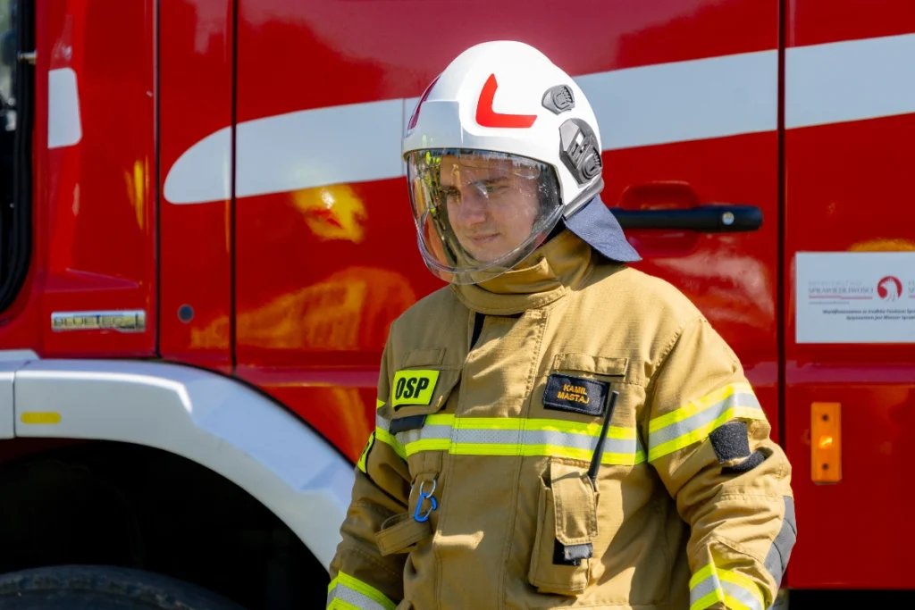 Volunteer firefighter in a white helmet with the visor down stands by a red fire engine