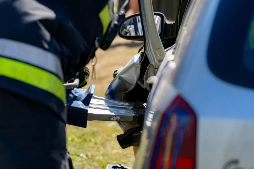 Firefighter in a dark uniform spreads bent metal at a car door with a hydraulic rescue tool, close-up