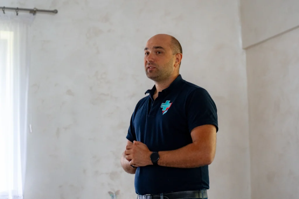 Training instructor in a navy polo shirt with the MED-POŻ logo addresses the room, close-up