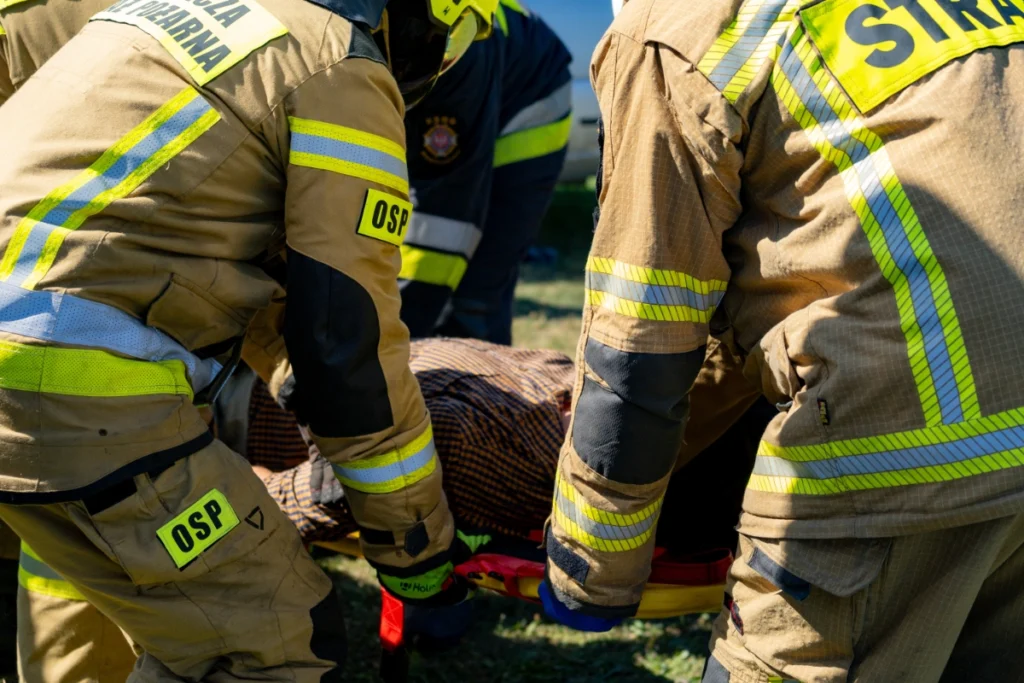 Volunteer firefighters hold a yellow spine board by its handles, with a casualty lying on it