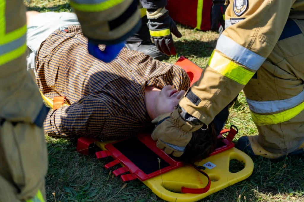Volunteer firefighter stabilises the head of a casualty lying on a yellow spine board on the grass