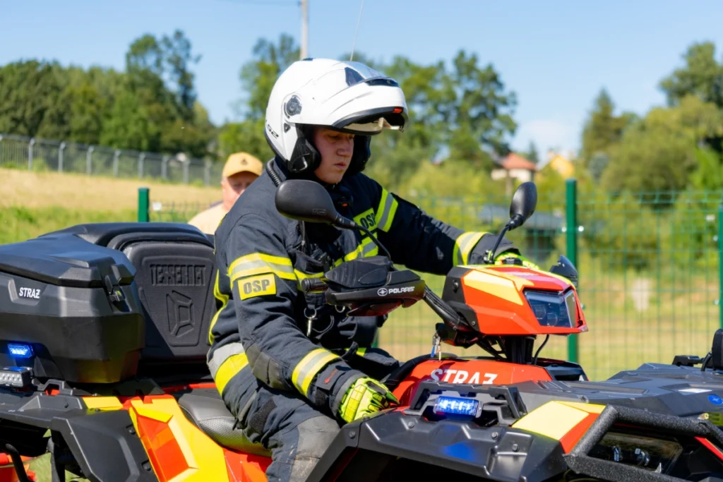 Volunteer firefighter in a white helmet sits at the handlebars of a rescue quad marked STRAŻ