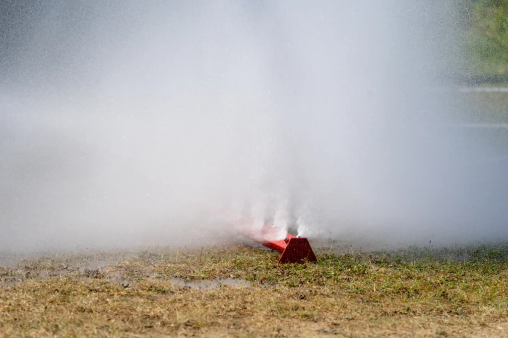 A red water curtain bar lying on the grass shoots a dense mist of water upwards