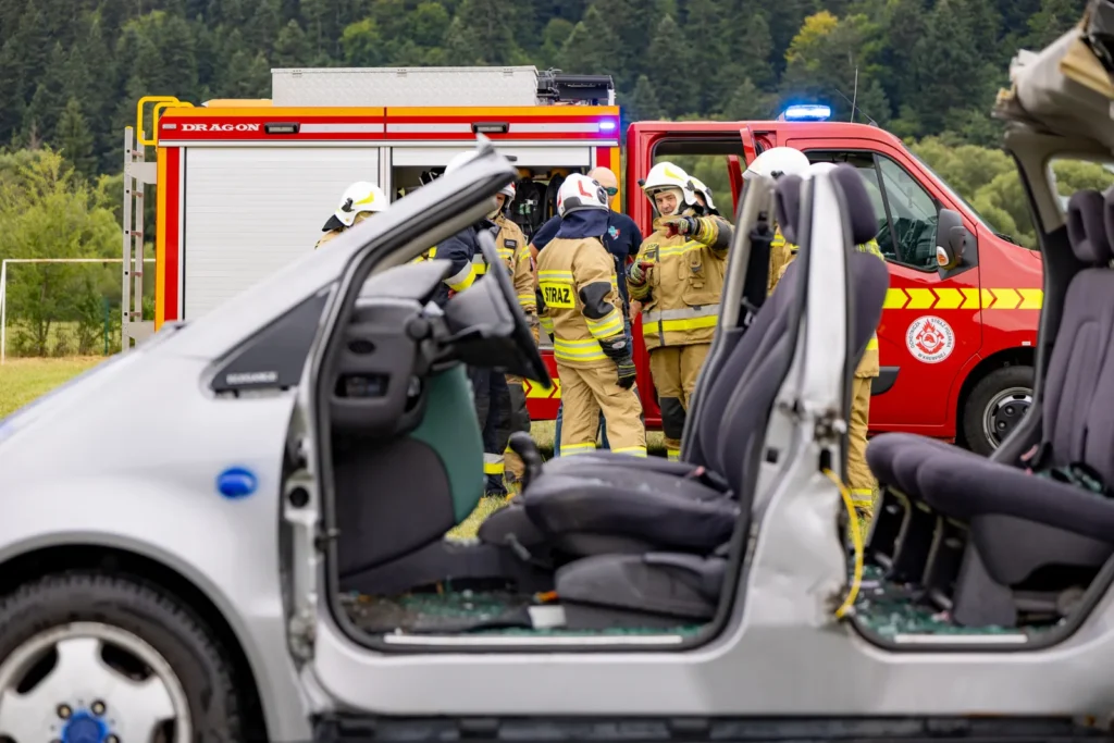 Strażacy naradzają się przy wozie bojowym, na pierwszym planie auto z wyciętymi drzwiami