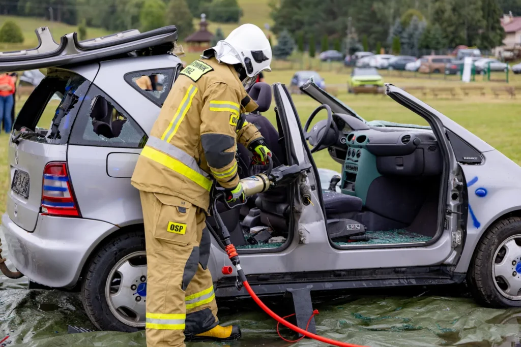 Strażak OSP rozpiera narzędziem hydraulicznym słupek drzwi w rozciętym samochodzie osobowym