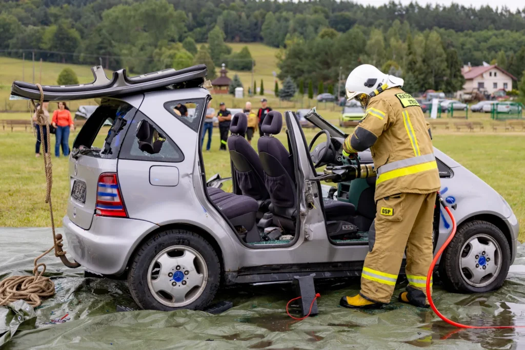 Strażak operuje rozpieraczem hydraulicznym przy fotelu kierowcy w aucie z odciętym dachem
