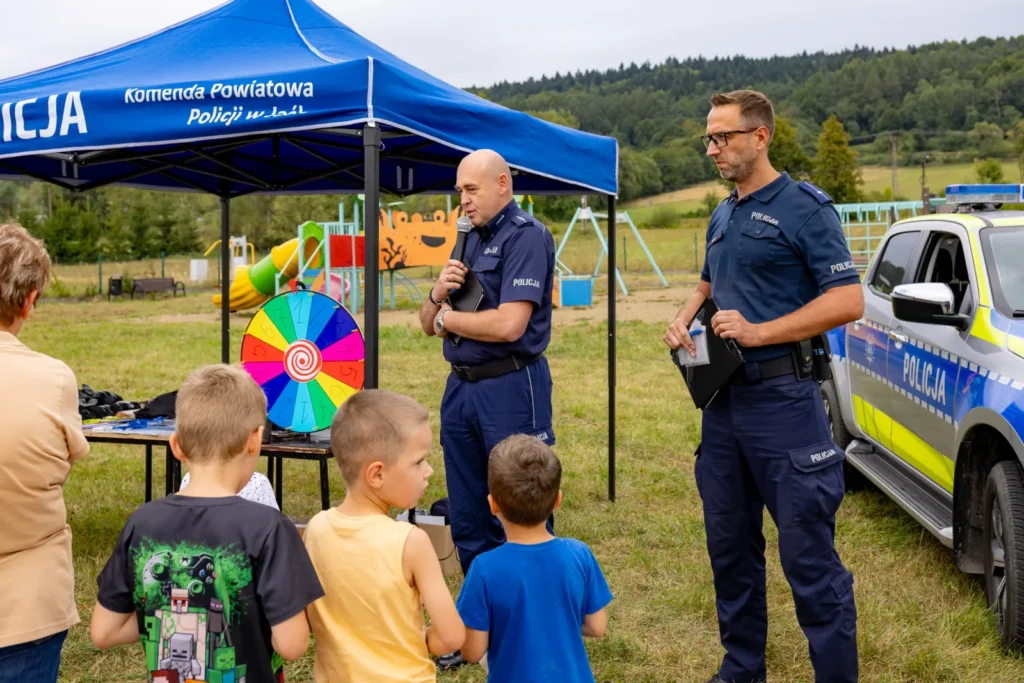 Policjanci przy namiocie Komendy Powiatowej Policji w Jaśle rozmawiają z grupą dzieci