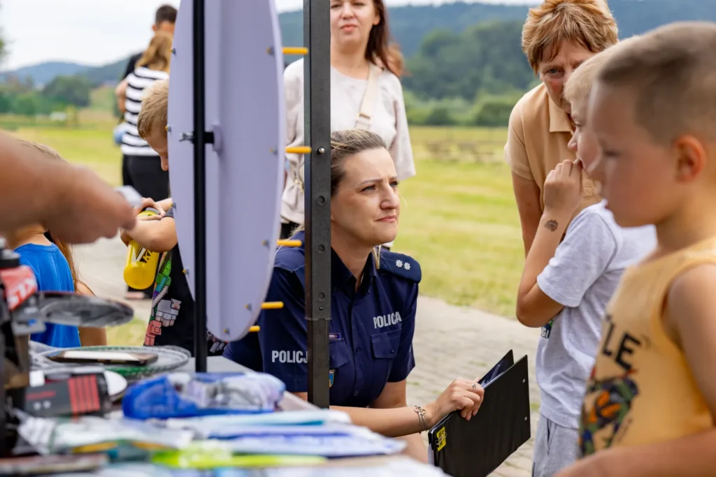Policjantka za stołem z odblaskami i gadżetami rozmawia z dziećmi podczas pikniku